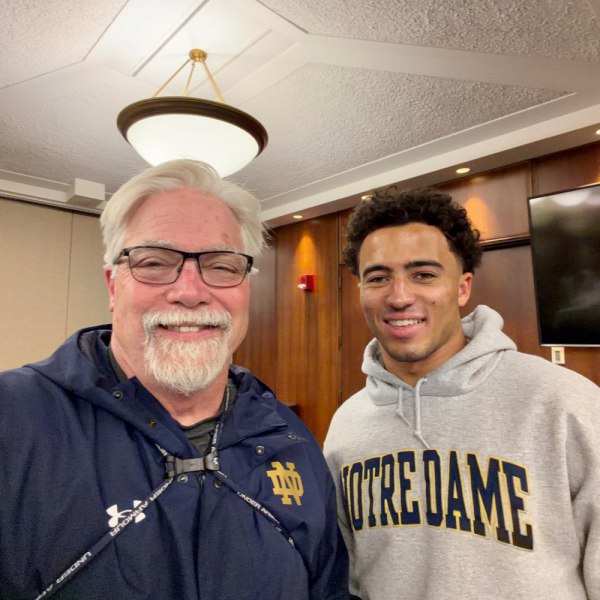 Two smiling men wearing Notre Dame clothing pose for a photograph.